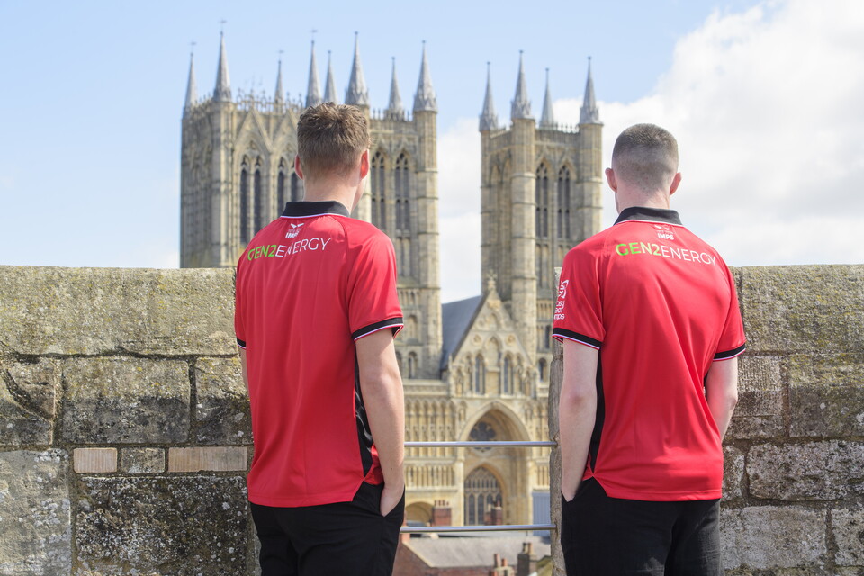 Two men stand wearing red shirts looking away from the camera towards a cathedral