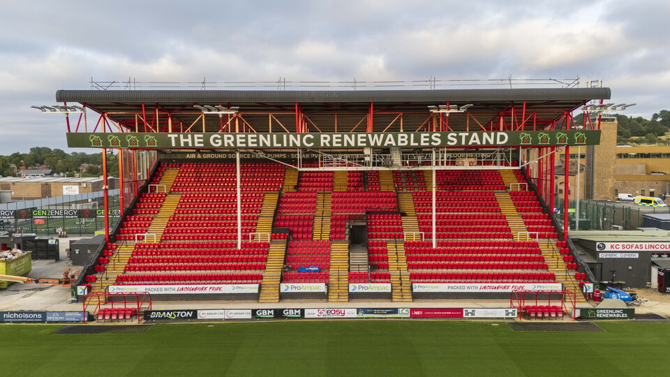 A view of a football stand with new red seats. Thee is a sign which reads "Greenlinc Renewables Stand"