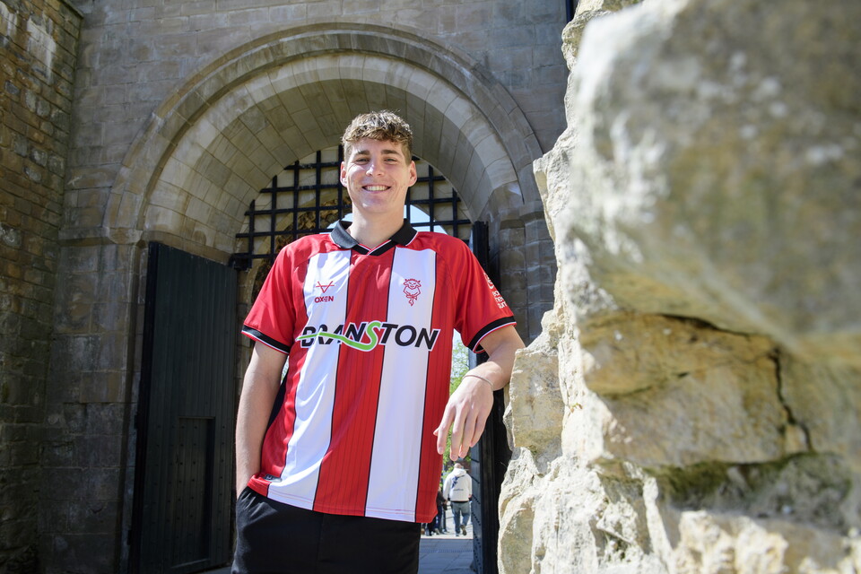 A man stands in a red and white striped football top in front of an arch