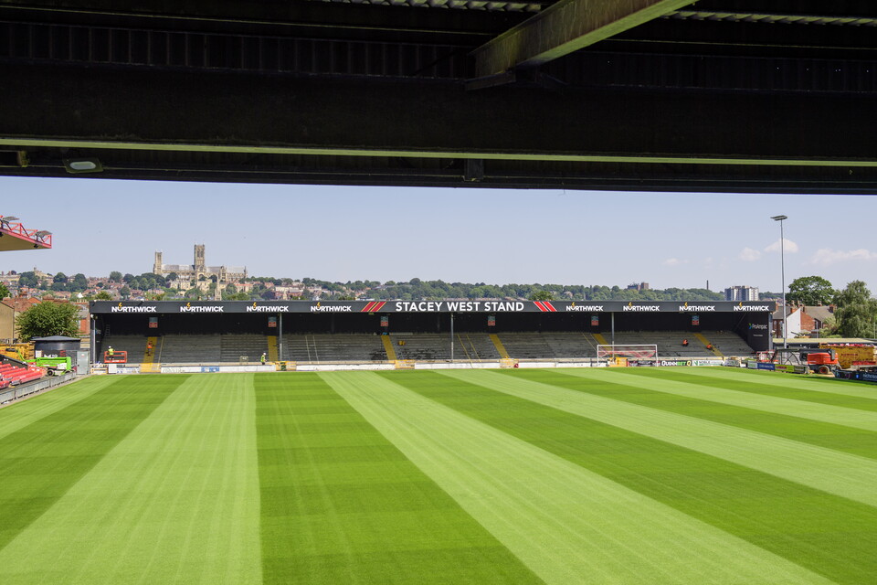 A view of a football stand where all the seats have been removed. There is a sign on the roof which says "Stacey West Stand"