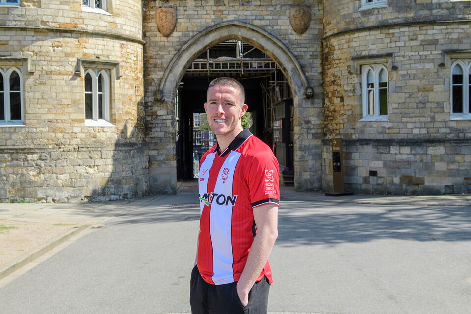A man wears a red and white football shirt in front of Lincoln Castle.