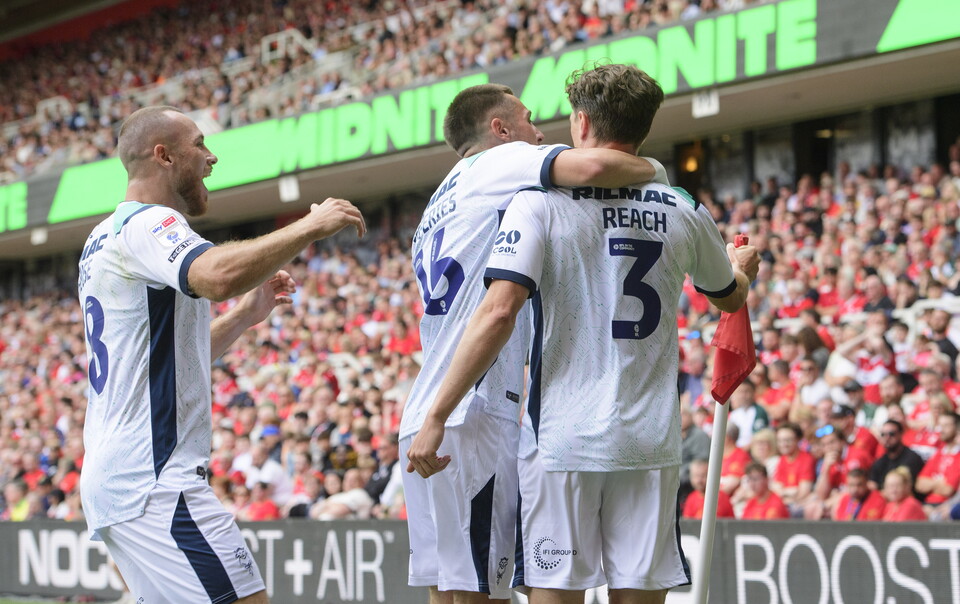 Three players in white football shirts come together to celebrate a goal