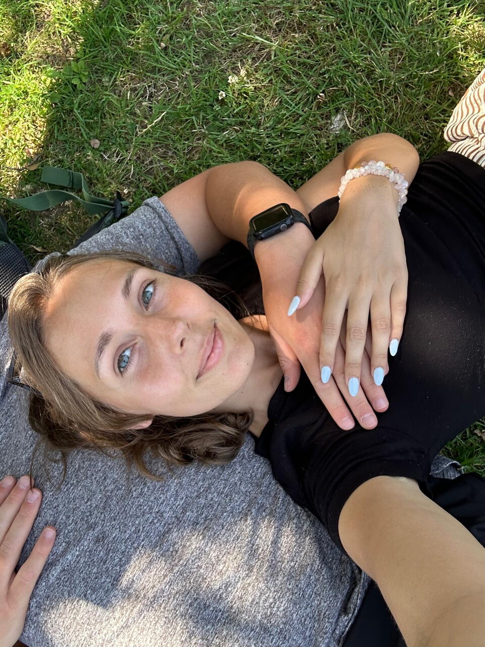 A woman lays on grass. She is smiling and wearing a black top.