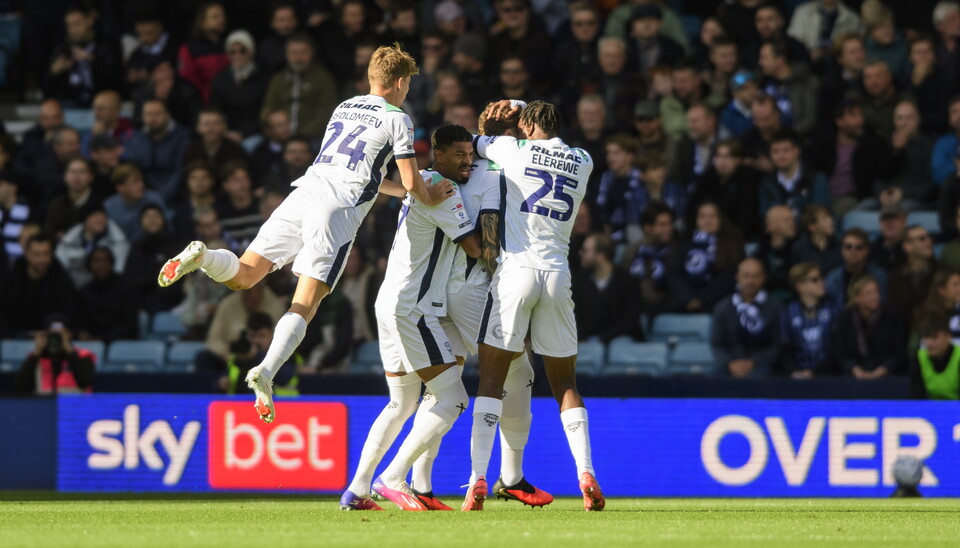 Several footballers in white jump on each other to celebrate a goal
