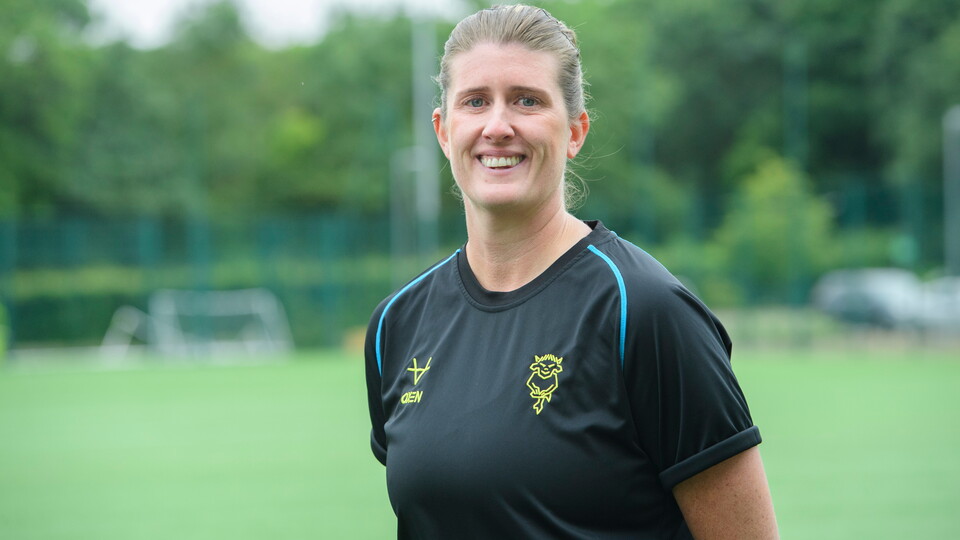 Lincoln City Women head coach Charlotte Dinsdale poses on a football pitch. She is wearing a black training top.