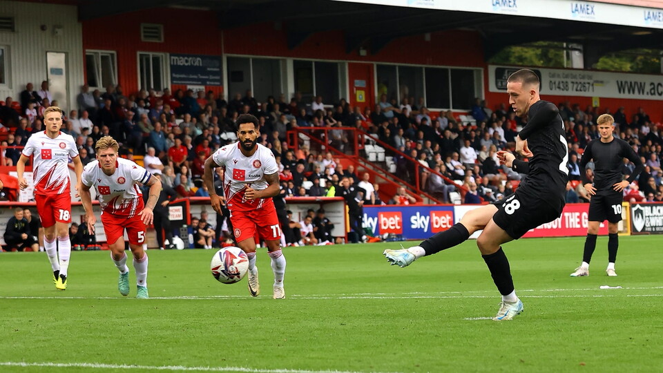 Jack moylan, wearing an all black kit, kicks the ball with his right foot to score a penalty against Stevenage.