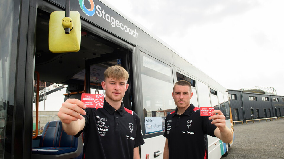 JJ McKieranan and Dom Jefferies, wearing black shirts, stand in front of a Stagecoach bus holding up red season membersship cards
