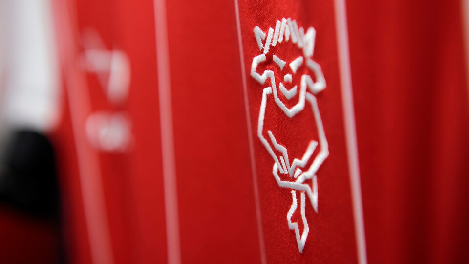 A close up of the Lincoln City club badge on a home shirt. The badge is a white outline of an Imp on a red shirt. 