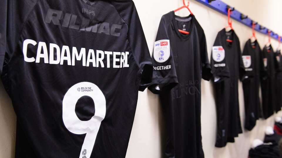 A close up of black shirts hung in a changing room. On the left the shirt is turned round and "Cadamarteri 9" is visible