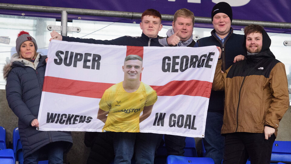 Five people hold up a flag which reads "Super George Wickens in goal".