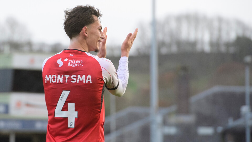 Lewis Montsma applauds fans. He is pictured from behind and you can see the back of his red football shirt which says "Montsma 4"