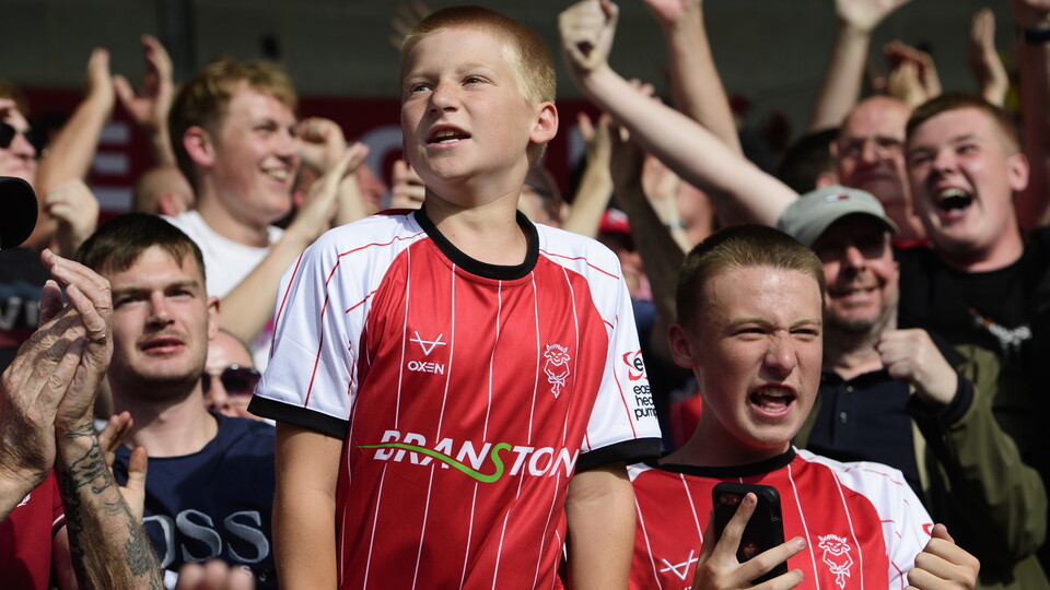 A Lincoln City fan in a red shirt celebrates a goal