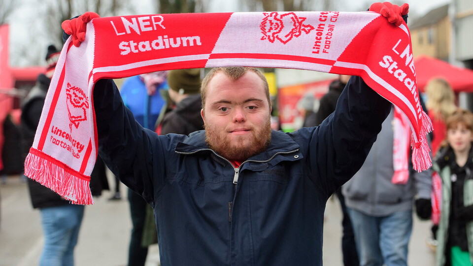 A Lincoln City supporter raises a scarf in the Fan Village
