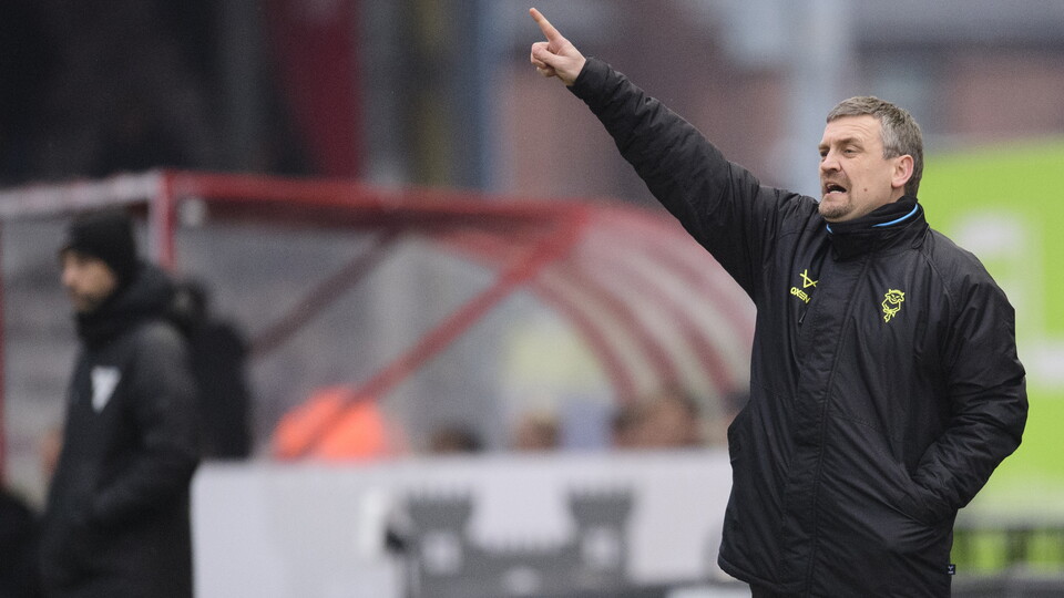 Michael Skubala gestures with his right hand. He is wearing a black jacket and tracksuit bottoms.