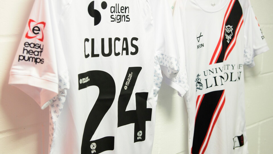 A white shirt hung up in a changing room. On the back is "Clucas 24"