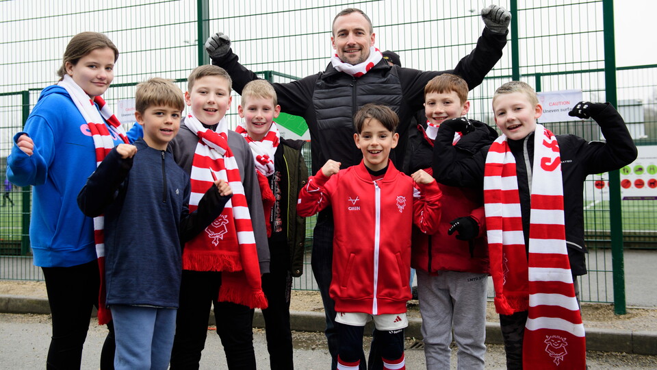 A group of Lincoln City supporters pose for a photo. They are all raising their aims in celebration.