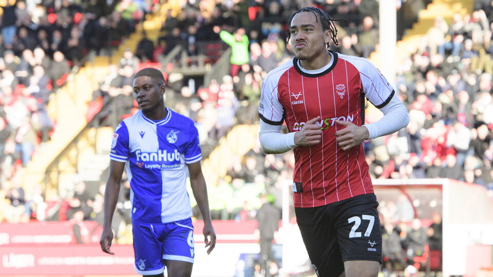 Jovon Makama wheels away to celebrate after scoring a goal. He is wearing a red football top.