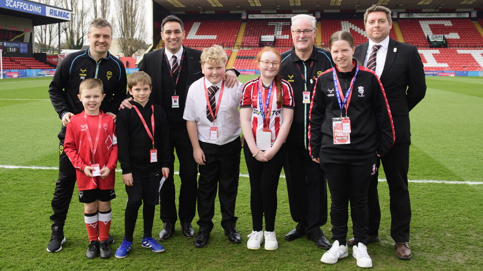 A group of adults and children pose by the side of a football pitch