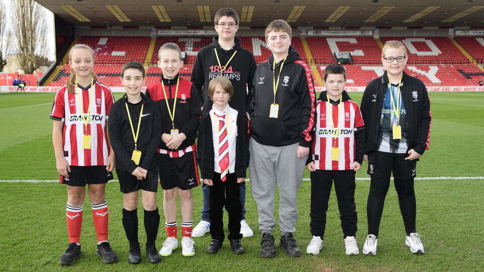 A group of children pose by a football pitch.