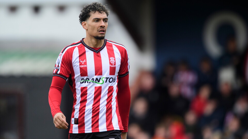 Tyler Walker stands wearing a football shirt with red and white stripes. On the front is Branston.