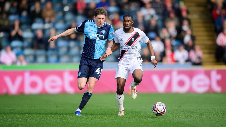 Tendayi Darikwa in possession of the football for Lincoln City at Adams Park with Adam Reach of Wycombe Wanderers running next to him.