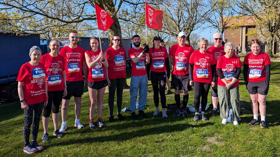 A group of runners pose for a photo. They are all wearing red shirts and black shorts.