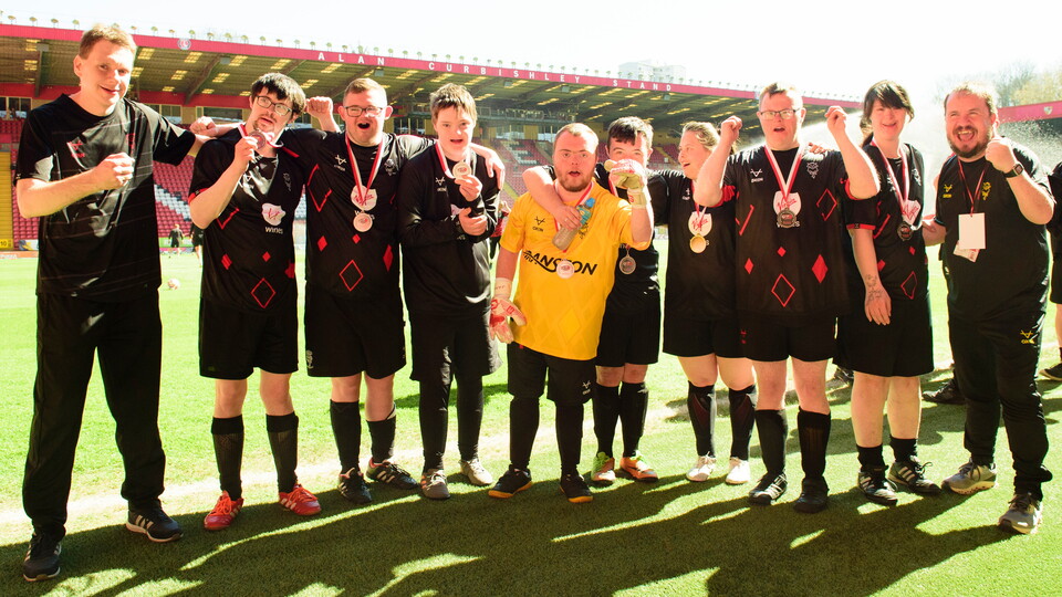 A group of people pose on a football pitch