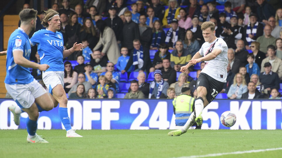 Erik Ring, in white shirt and black shorts, kicks the ball to score against Stockport County