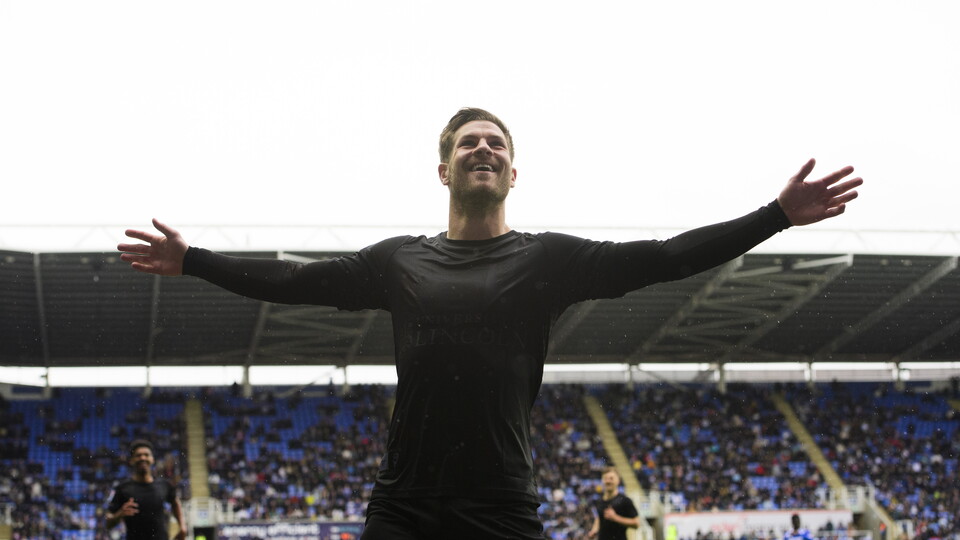 James Collins holds his arms aloft in celebration after scoring a goal. He is wearing all-black shorts and shirt.