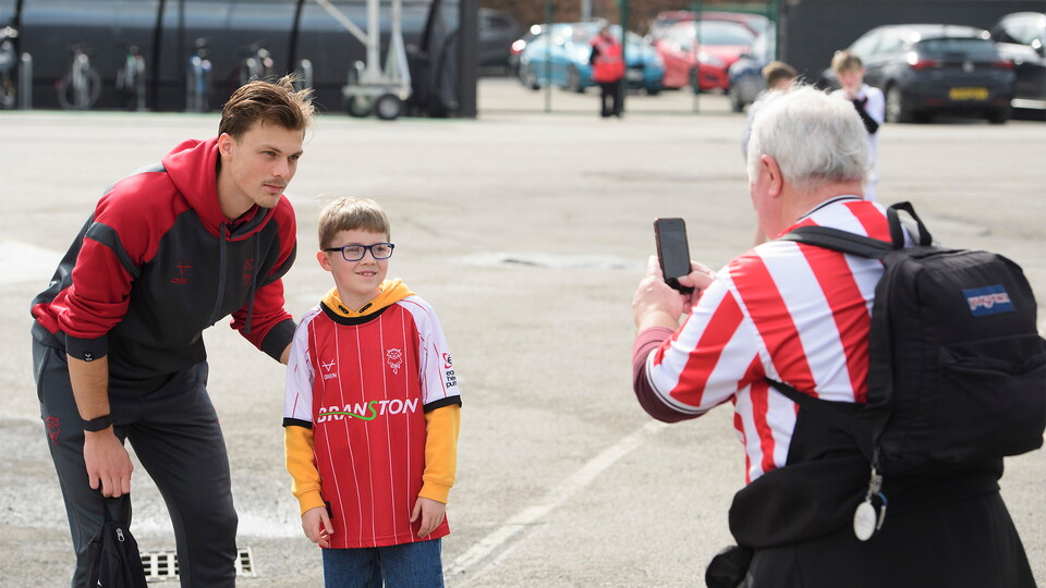 Erik Ring of Lincoln City poses for a photograph with a fan poses for a photograph with a fan outside the LNER Stadium.