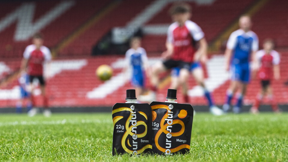 Two Purendure sachets in front of people playing football