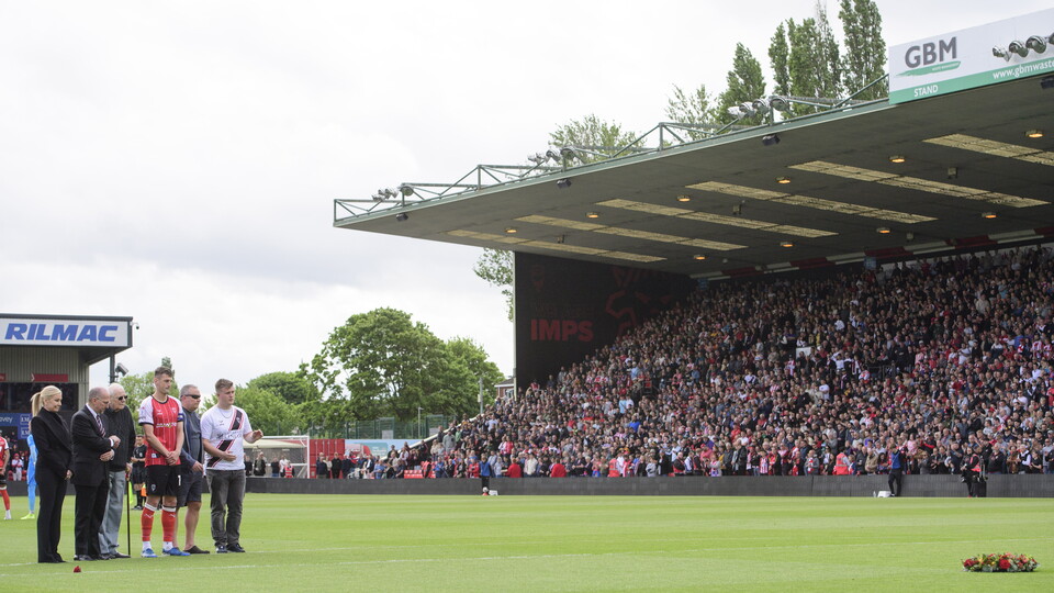 A group of people stand to observe a minute's silence.