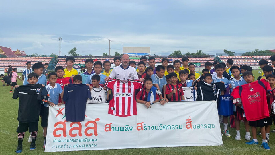 A man holding a Lincoln City shirt in a group photo with some children.