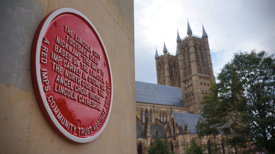 A close up of a red plaque on a wall. In the background is Lincoln Cathedral