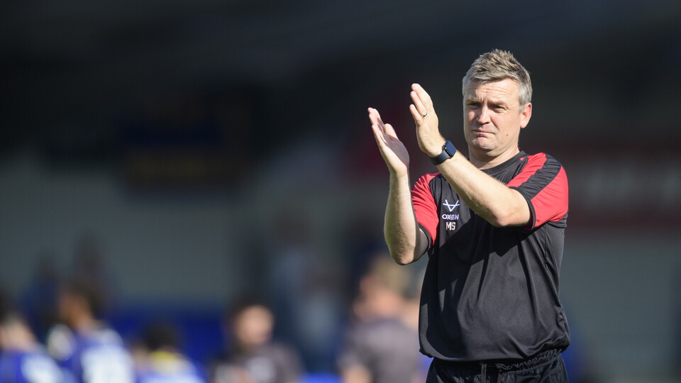 Head coach Michael Skubala applauds fans. He is wearing a black t-shirt.