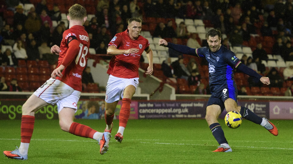 James Collins, wearing all blue, kicks the ball with his left foot to score a goal.