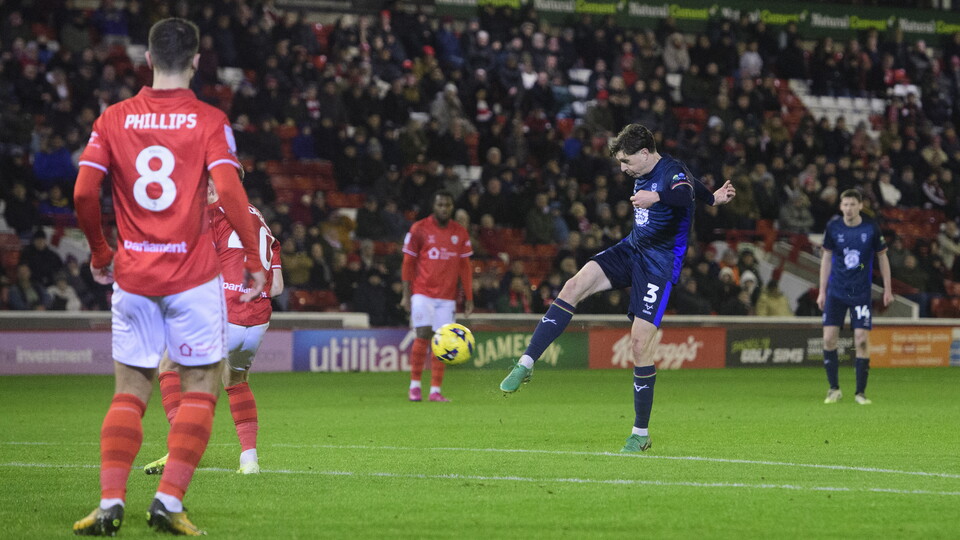 Adam Reach kicks the ball towards goal to score for Lincoln City.