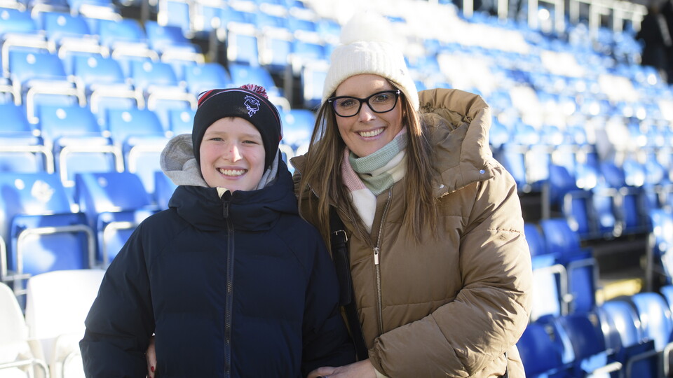A child and a woman stand in front of a stand of blue seats
