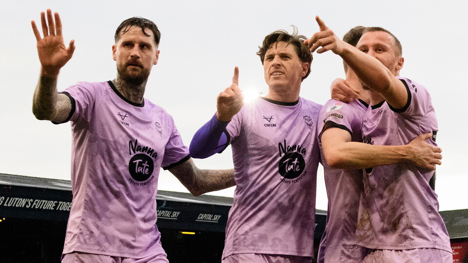 Three football players celebrate a goal wearing a purple shirt