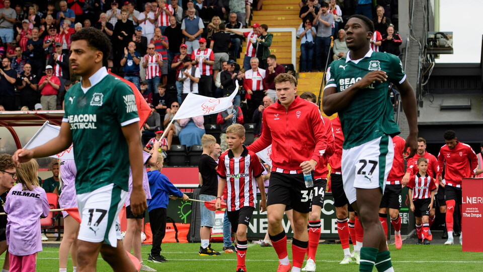 Freddie Draper of Lincoln City walks out onto the pitch with a matchday mascot prior to the EFL Sky Bet League One match between Lincoln City and Plymouth Argyle at LNER Stadium, Lincoln.
