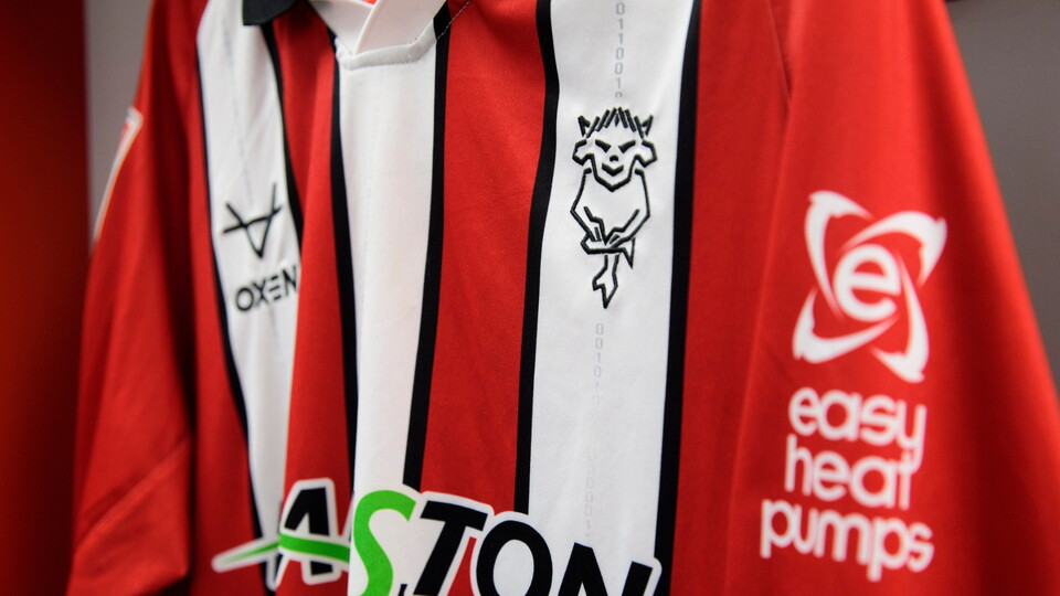 A red and white Lincoln City shirt hung up in a changing room.