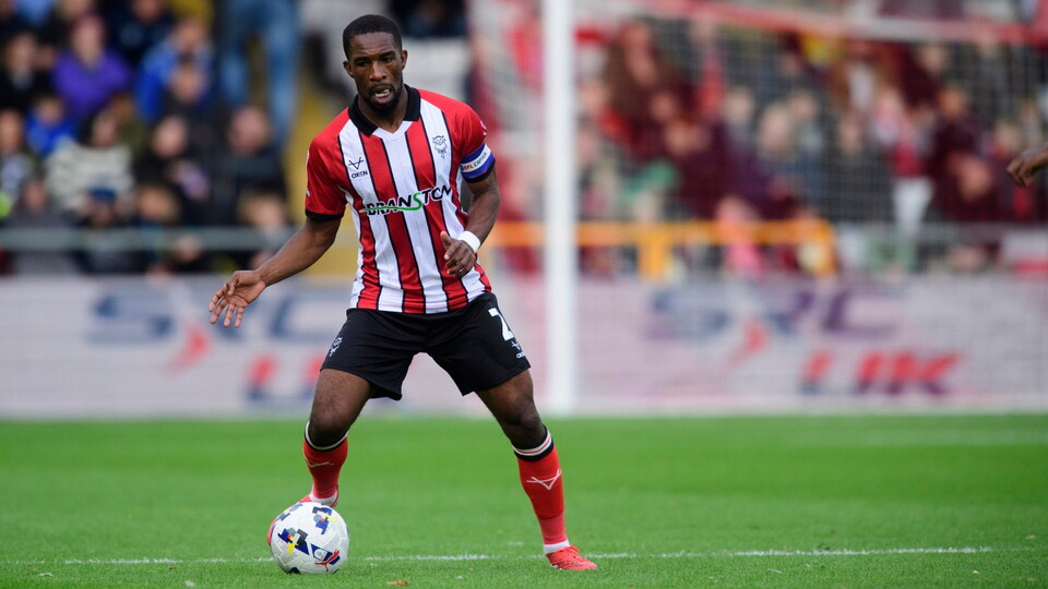 Football player in a red and white striped shirt dribbles the ball on a green pitch. 