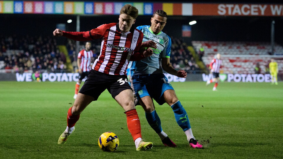 Two football players compete for control of the ball during a night match. The player in red and white attempts to shield the ball from the other in blue and green.
