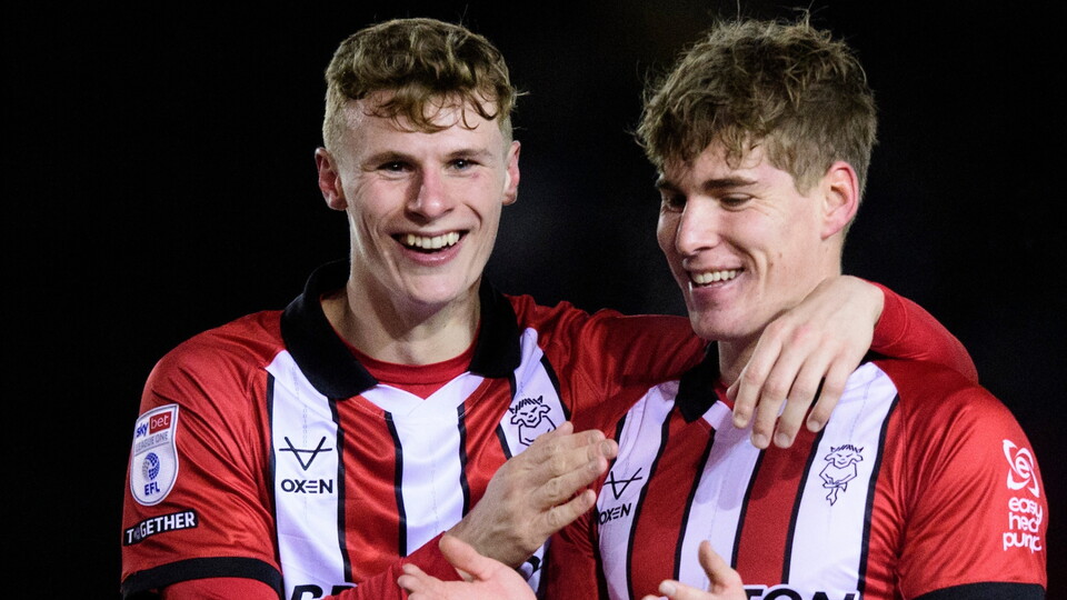 Two football players celebrate together, wearing red and black striped jerseys.