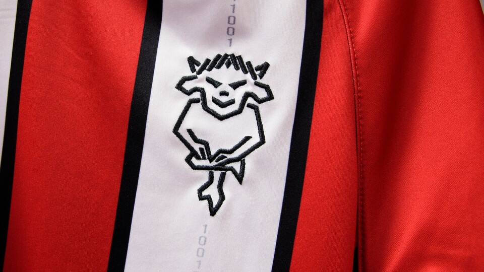 Close-up of a red and white striped fabric with a black embroidered Imp emblem on the white stripe.