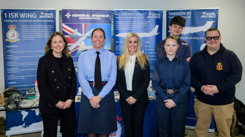 Group of six people standing in front of Royal Air Force and General Atomics posters. Some wear uniforms, others are in civilian attire. They are smiling, creating a positive and professional atmosphere.