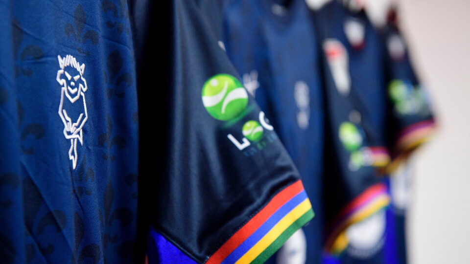 Navy blue sports jerseys with colorful striped sleeves hang in a row.