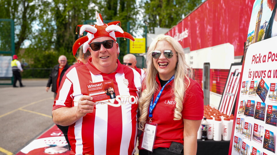 A man in a red and white shirt holding a ticket stood next to a woman in a red shirt. Both are smiling.
