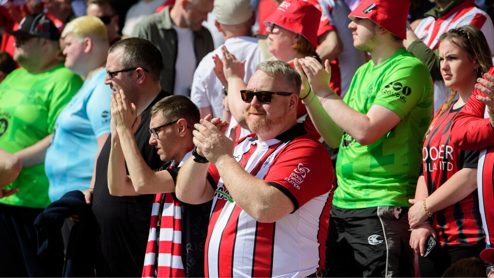 A man wearing a red and white striped shirt and sunglasses, smiling while standing outdoors.