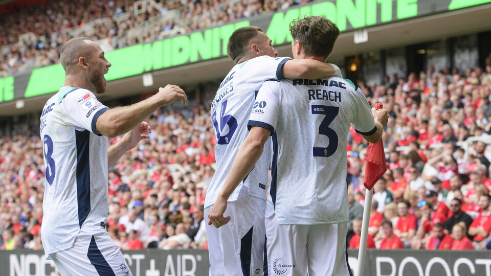 Three players in white football shirts come together to celebrate a goal